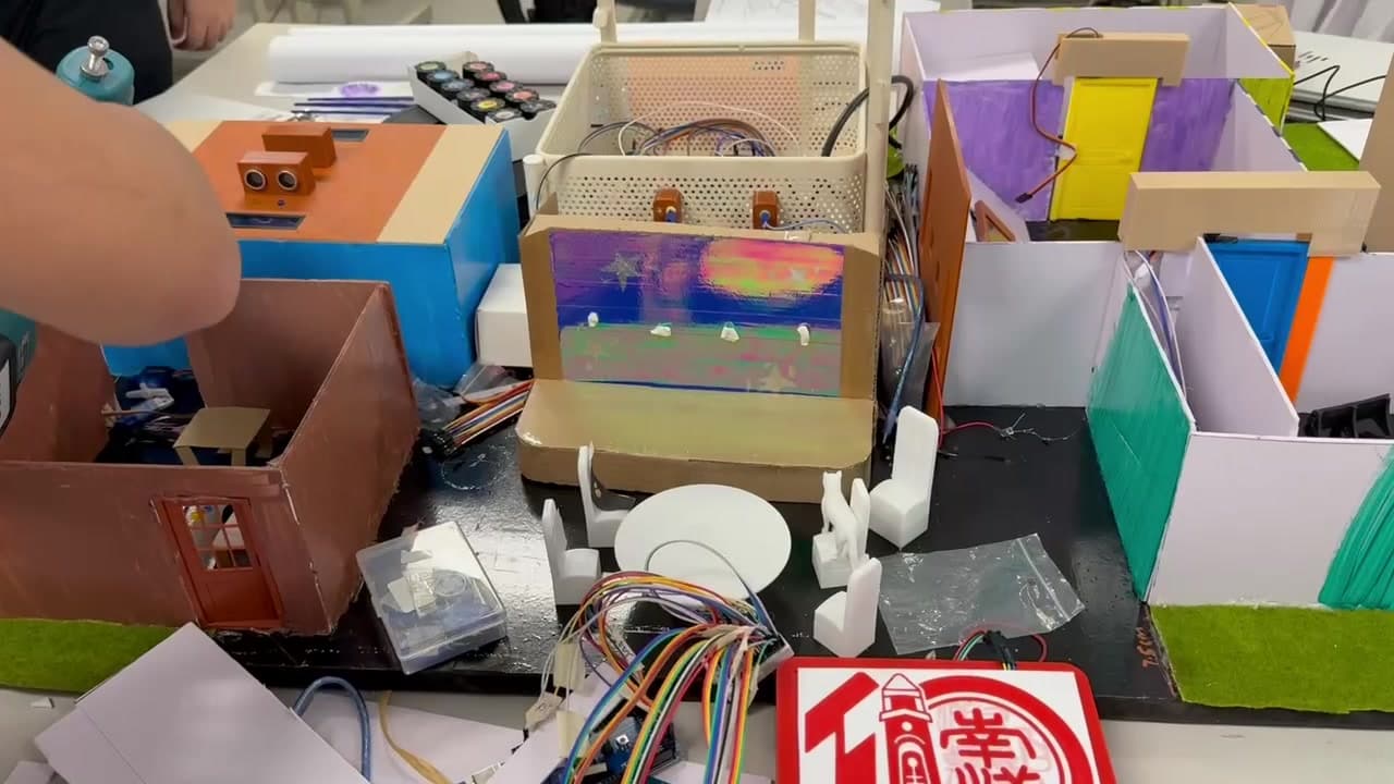 Colourful miniature rooms with sensors, white 3D printed furniture and connected wiring; no faces pictured
